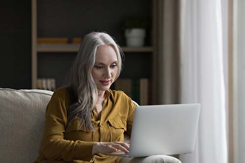 a woman sits on her couch with her laptop participating in telehealth addiction treatment