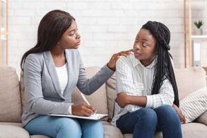 a woman taking notes consoles another woman while suggesting person-centered therapy